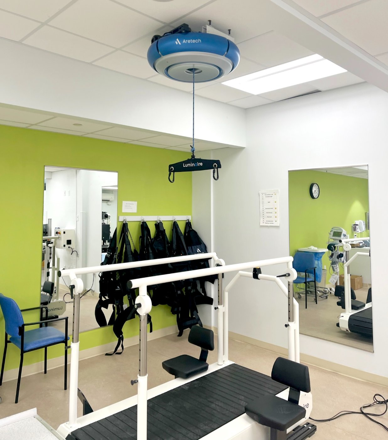 A Luminaire BWS treadmill system in a therapy gym — overhead robot, harnesses, and parallel bars