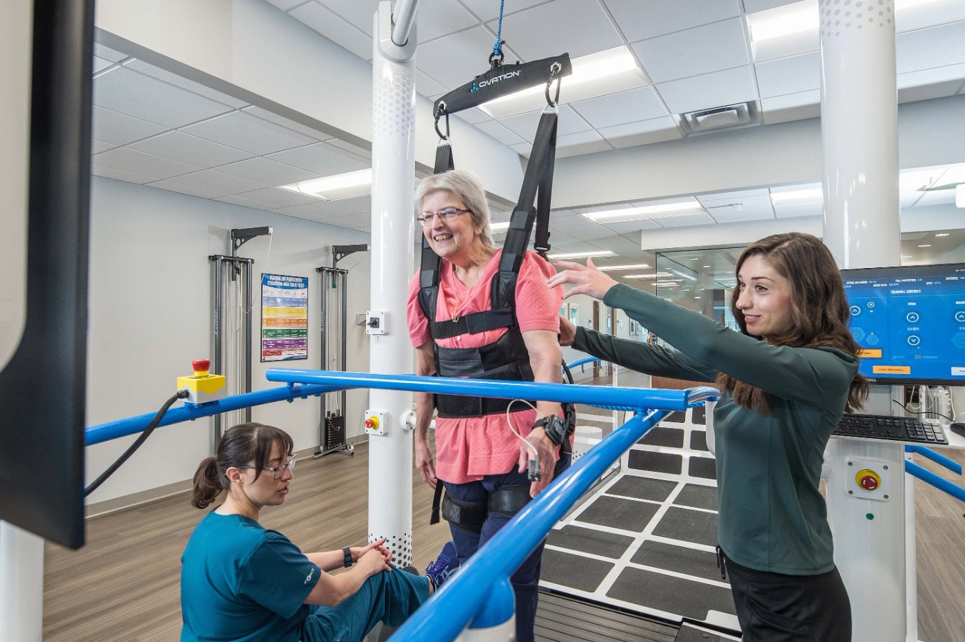 Patient walking on Ovation while a therapist coaches from beside the treadmill