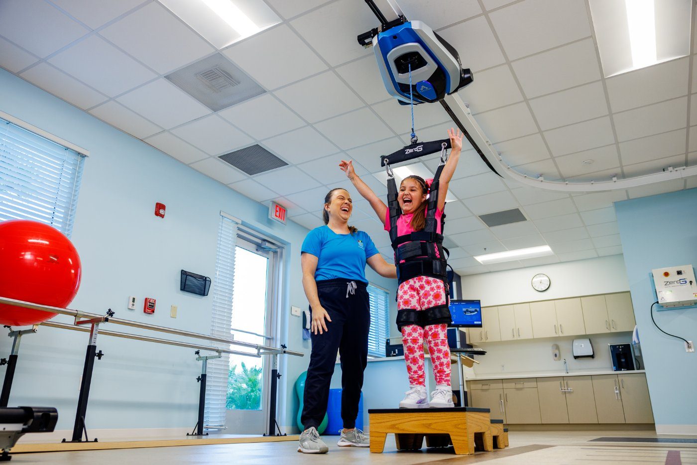 Child cheering in a ZeroG harness during a step exercise with a clinician