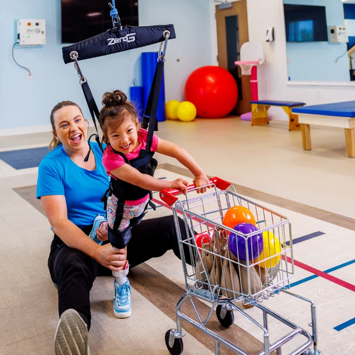 Child in a ZeroG sling pushing a toy cart during play-based therapy